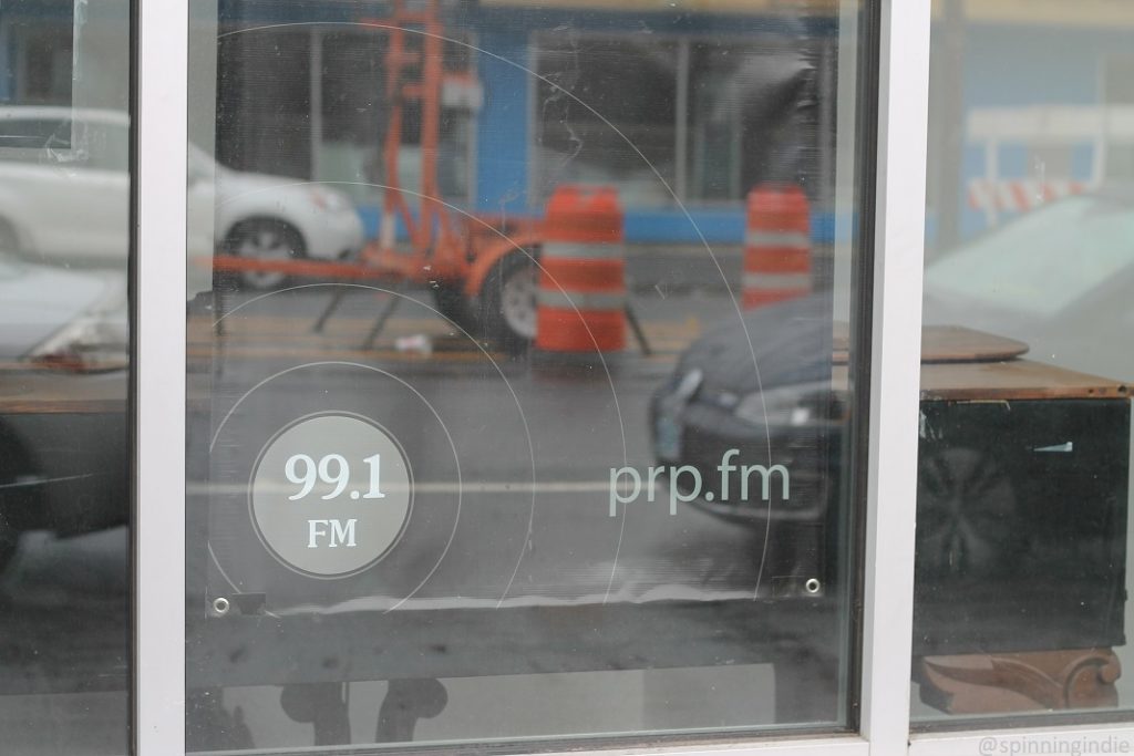 Portland Radio Project sign in ground floor window, reflecting view of street. Photo: J. Waits