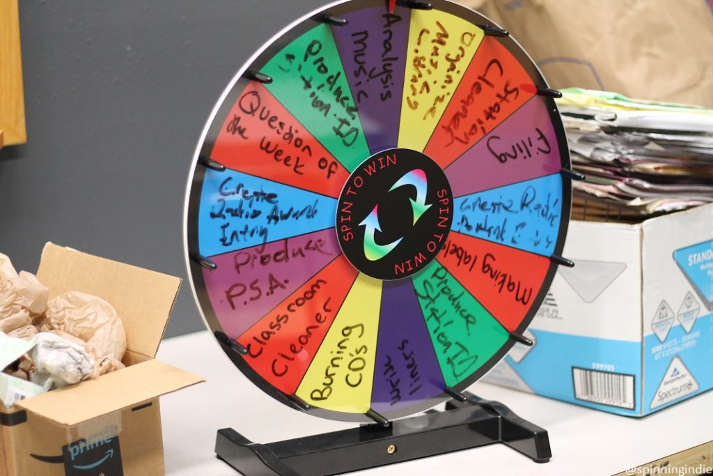 KMIH task wheel, with chores and tasks hand written onto the spinning wheel: "question of the week," "produce PSA," "classroom cleaner," "burning CDs," "filing" and more. Photo: J. Waits/Radio Survivor