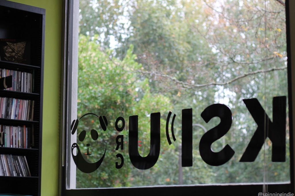 KSPU studio, looking out large window with KSPU logo. Shelf of CDs to the left. Photo: J. Waits/Radio Survivor