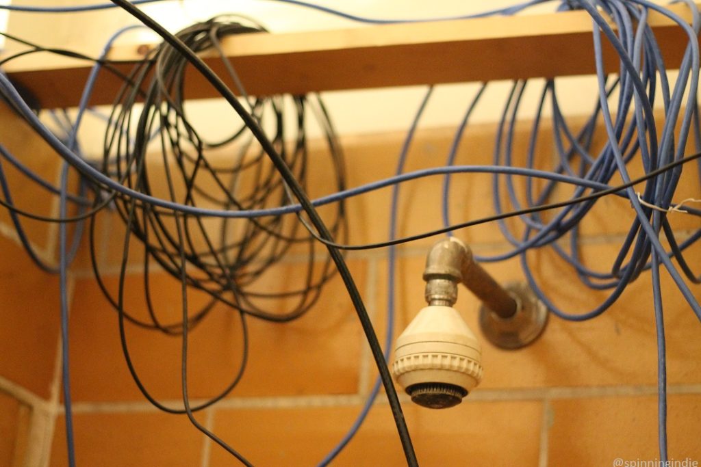 Old shower fixture on wall, with cables overhead at LPFM radio station Space 101.1 FM. Photo: J. Waits/Radio Survivor
