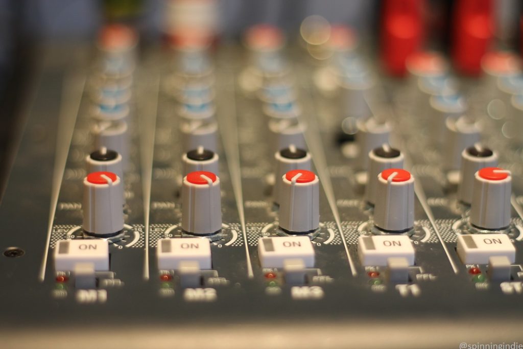 Close up on audio mixing board dials and a series of "on" buttons at KBFG's Shack location. Photo: J. Waits/Radio Survivor