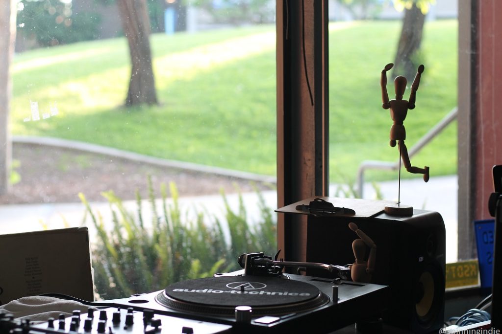 View of campus from college radio station KSDT studio. Pictured: turntable, audio equipment, large window overlooking grass, trees. Photo: J. Waits/Radio Survivor