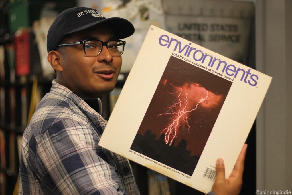 Emanuel Castro Cariño holds up "Environments: Totally New Concepts in Sound-Disc 4" LP in KSDT music library. LP has photo of lightning in the center. Photo: J. Waits/Radio Survivor