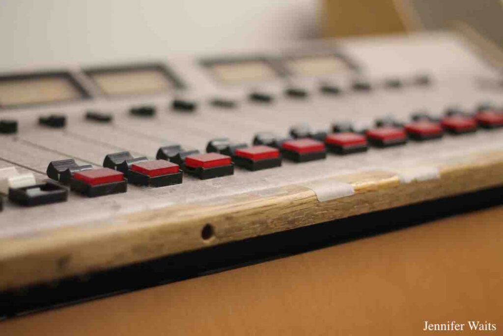 Older radio station mixing board at college radio station WCDB. Row of red square buttons visible and board is framed in wood. Photo: J. Waits