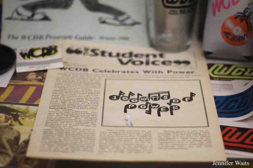 Memorabilia from college radio station WCDB inside trophy case. Pictured: WCDB matchbook, "Student Voices" newsletter, WCDB stickers, and a logo'd pint glass. Photo: J. Waits