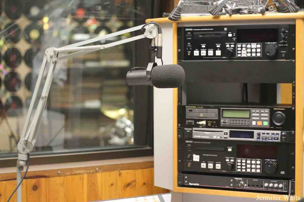 Studio at college radio station WRPI. Boom with microphone is in front of window facing another studio. Next to the microphone is a rack of audio equipment, including CD players and other components. Photo: J. Waits
