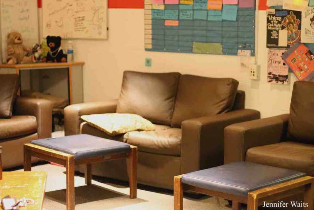 Photo of college radio station WRPI. Several brown leather couches and chairs, with matching footstools. Teddy bears on table in background. Wall of flyers and a blue cardboard sign on wall has square grids for the program schedule. Photo: J. Waits