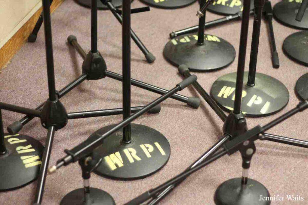 Photo of black microphone stands with the letters W R P I spray painted in yellow on their bases. Photo: J. Waits