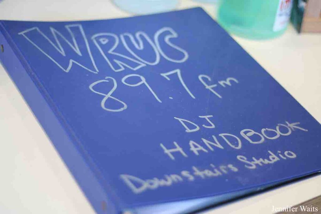 Photo of blue binder. Handwriting in silver marker on the cover reads: "WRUC 89.7 fm DJ Handbook Downstairs Studio." Photo: J. Waits