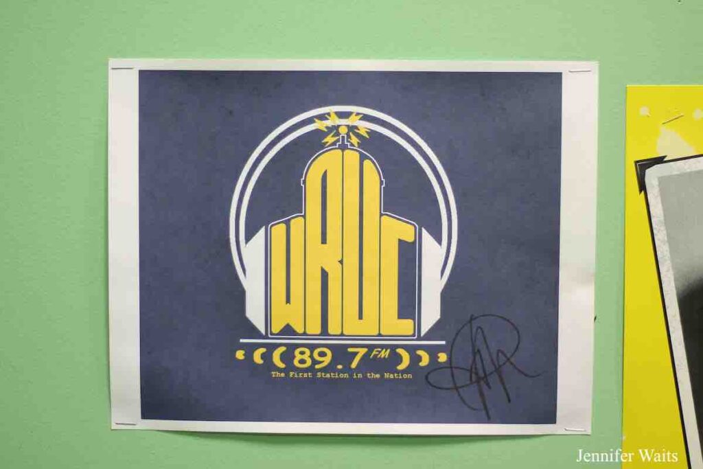 Photo of Flyer posted on wall at college radio station WRUC. Flyer has WRUC logo with headphones, with 89.7 FM underneath and the tagline: "The FIrst Station in the Nation." Photo: J. Waits