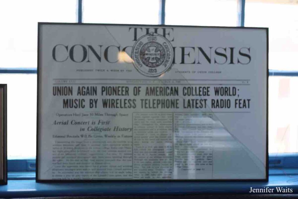 Photo of framed newspaper article, propped on a window sill. Article headline reads: "Union Again Pioneer of American College World; Music by Wireless Telephone Latest Radio Feat." Photo: J. Waits