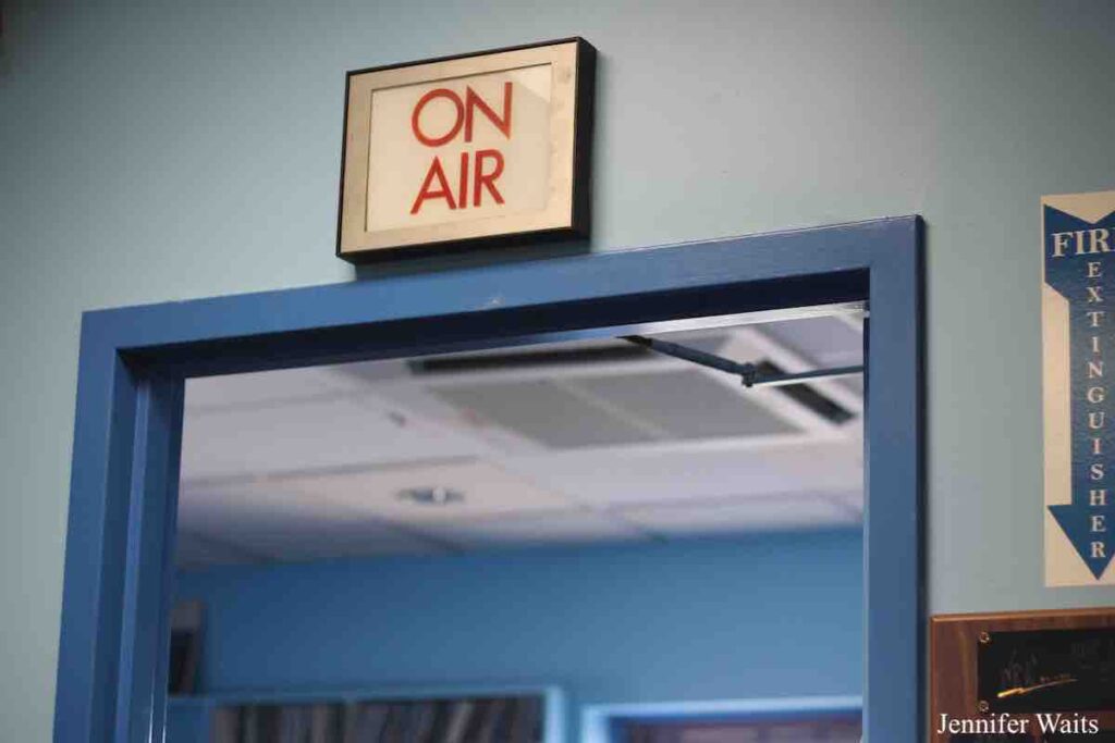 Photo of sign that says "On Air" in red letters. It's above a blue-framed doorway and there's a Fire Extinguisher sign to the right of the door. Photo: J. Waits