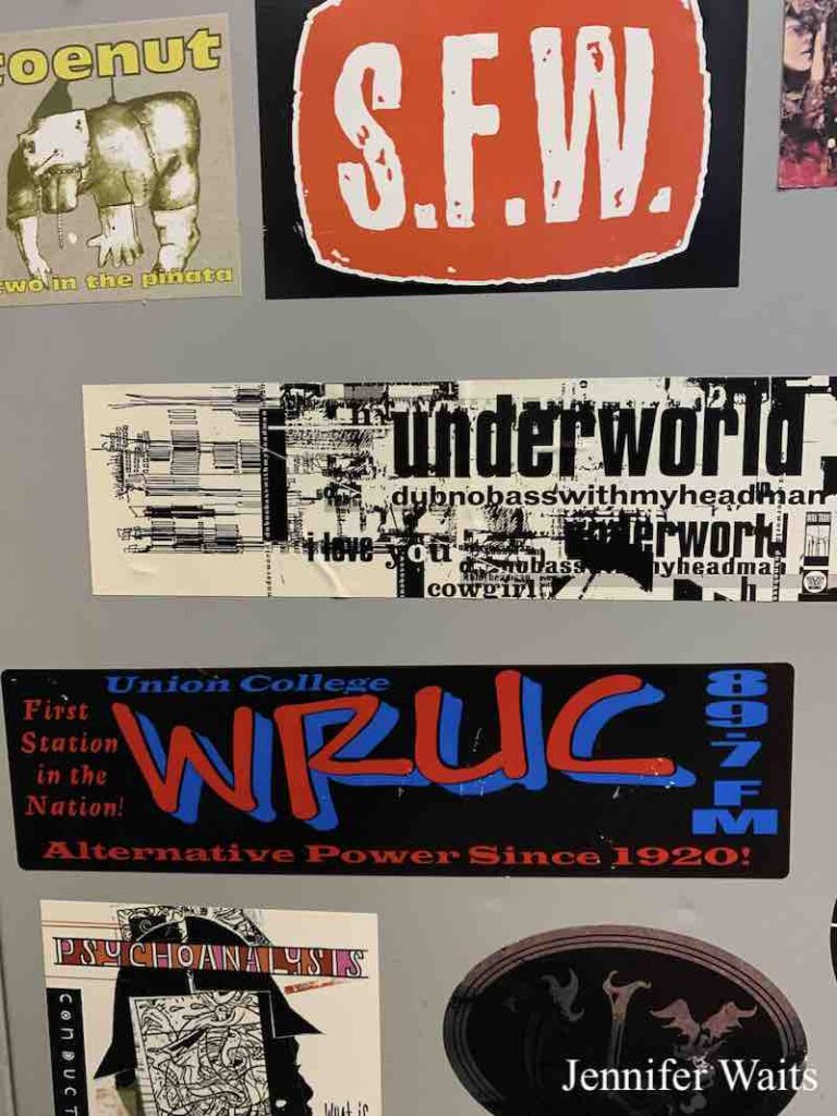 Photo of Stickers at college radio station WRUC. S.F.W., Underworld, and WRUC sticker in red, blue and black that reads: "Union College WRUC 89.7 FM - First Station in the Nation. Alternative Power since 1920!" Photo: J. Waits