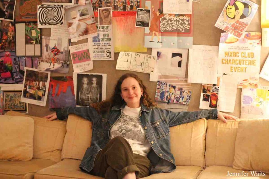 Photo of person sitting on couch at college radio station WXBC. Bulletin board behind the couch is full of hand-made flyers. Photo: J. Waits
