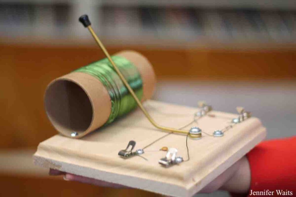 Photo of handmade crystal radio set at college radio station BSR. Green wire is wrapped around cardboard tube and it's attached to a piece of wood with wires and metal pieces on it. Photo: J. Waits