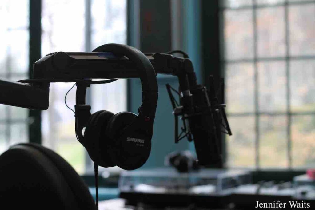 Photo of studio at college radio station WSLC. Pictured is a pair of headphones hanging on the boom arm of a microphone. In the background is a turntable. In the far background are windows overlooking the campus of Sarah Lawrence College. Photo: J. Waits