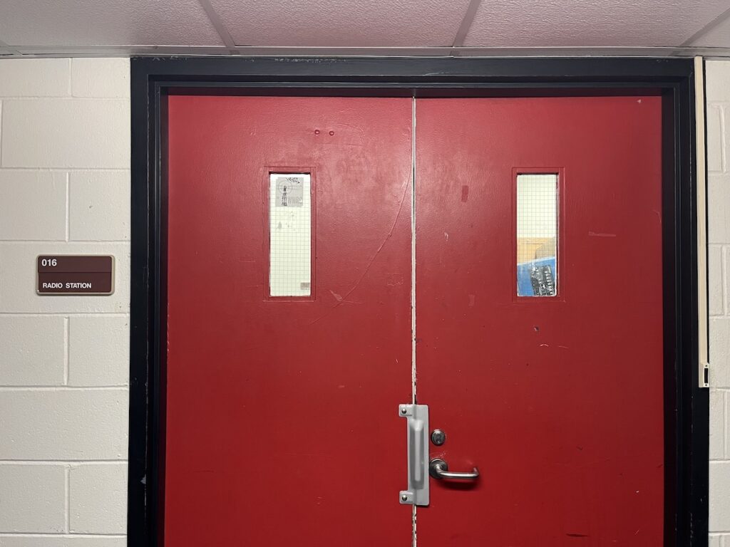 Haverford College radio station WHRC's entrance. Photo shows two red doors with small windows in each. Sign next to doors reads "radio station." 