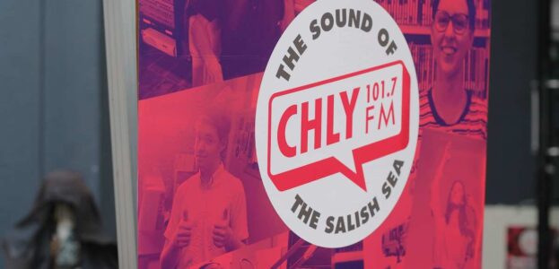 Radio Station Visit #192: Campus-Community Station CHLY-FM in Nanaimo, BC, Canada Photo of large promotional banner that has red-tinted photos surrounding the phrase: The Sound of CHLY 101.7 FM The Salish Sea. Photo by J. Waits