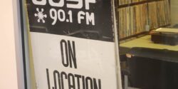 Photo of window entrance to campus and community radio station CJSF. Sign in window reads "CJSF 90.1 FM On Location" and one can see record albums in station in the background. Photo: J. Waits