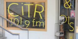 Photo of front of campus and community radio station CiTR. Pictured is the station's front window which has the letters "C-I-T-R" and "101.9 fm" written in yellow on the station's stdio window. Photo by J. Waits