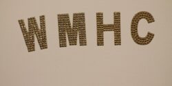 Gold letters W-M-H-C affixed to a white wall at Mount Holyoke College radio station WMHC. Photo: J. Waits