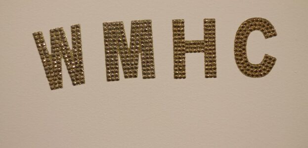 Gold letters W-M-H-C affixed to a white wall at Mount Holyoke College radio station WMHC. Photo: J. Waits