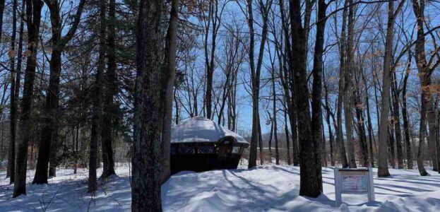 Photo of snowy forest with a yurt in the background. The yurt is the home of Hampshire College radio station Yurt Radio. Photo: J. Waits